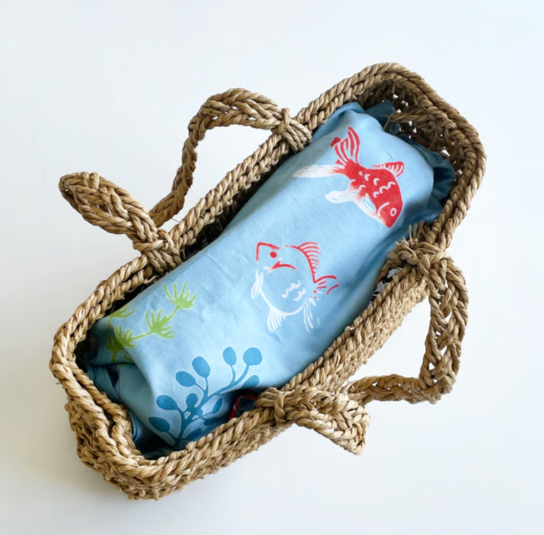 Woven basket with a tenugui featuring fish designs on a white background