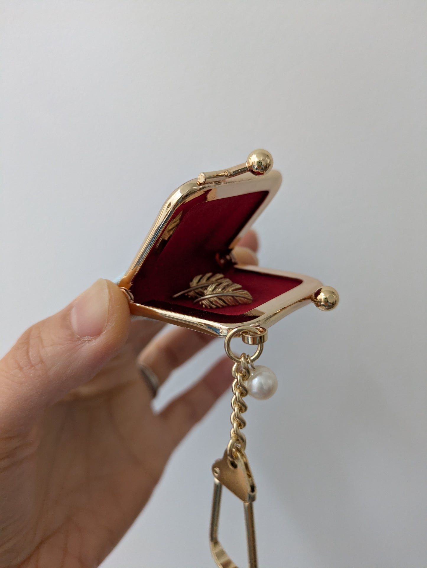 Gold and red decorative item held by a hand against a plain background
