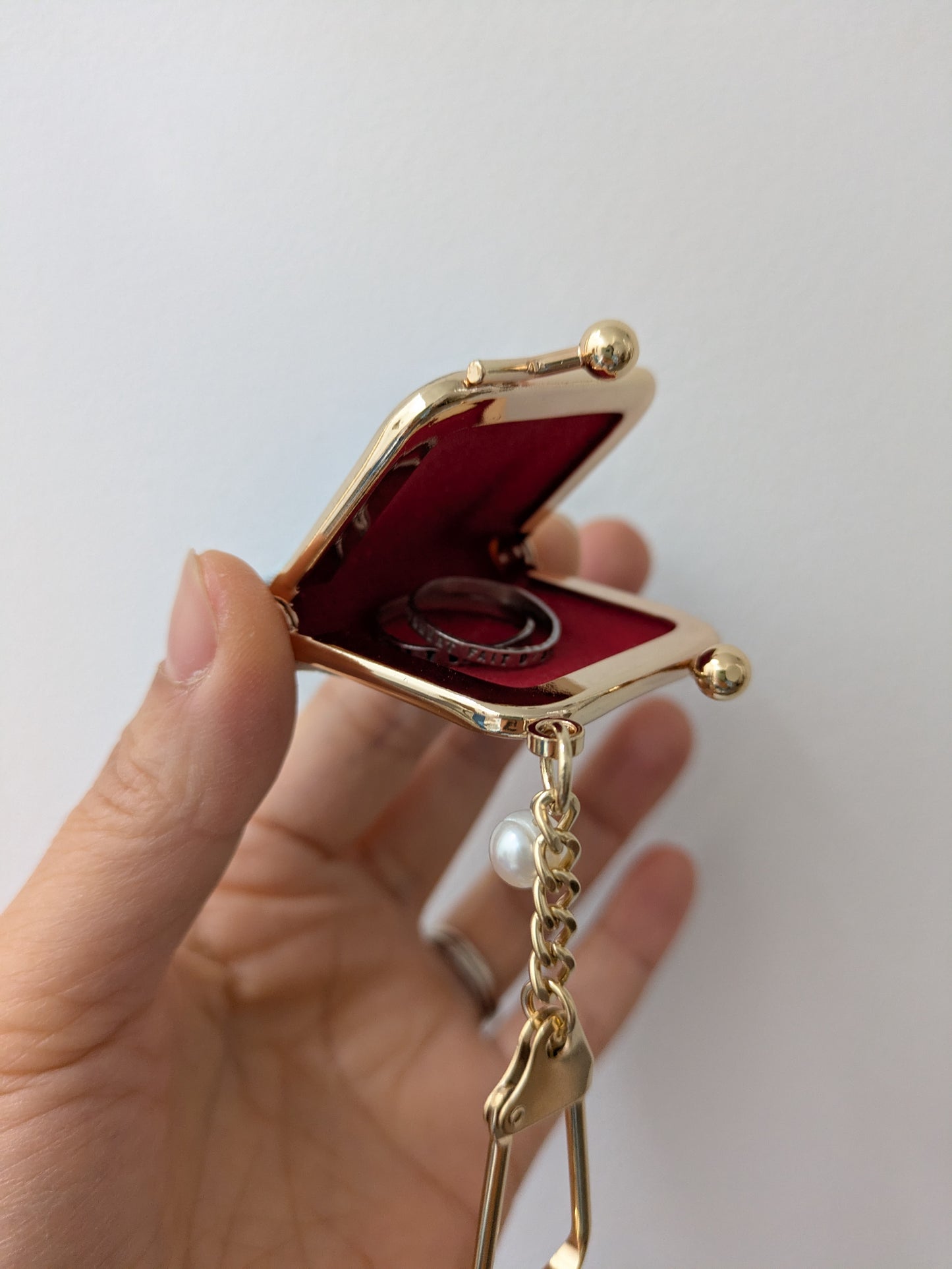 Gold jewelry box with red interior held by a hand against a white background