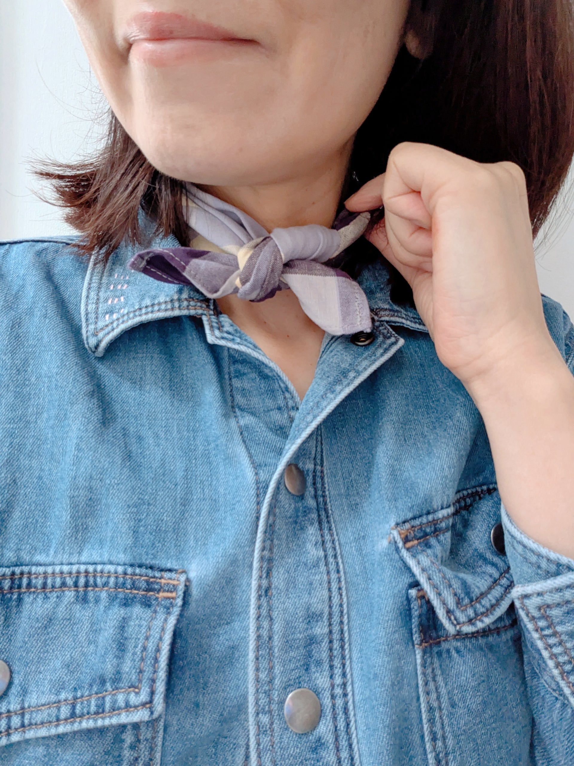 Person wearing a denim jacket with a purple scarf tied around their neck.