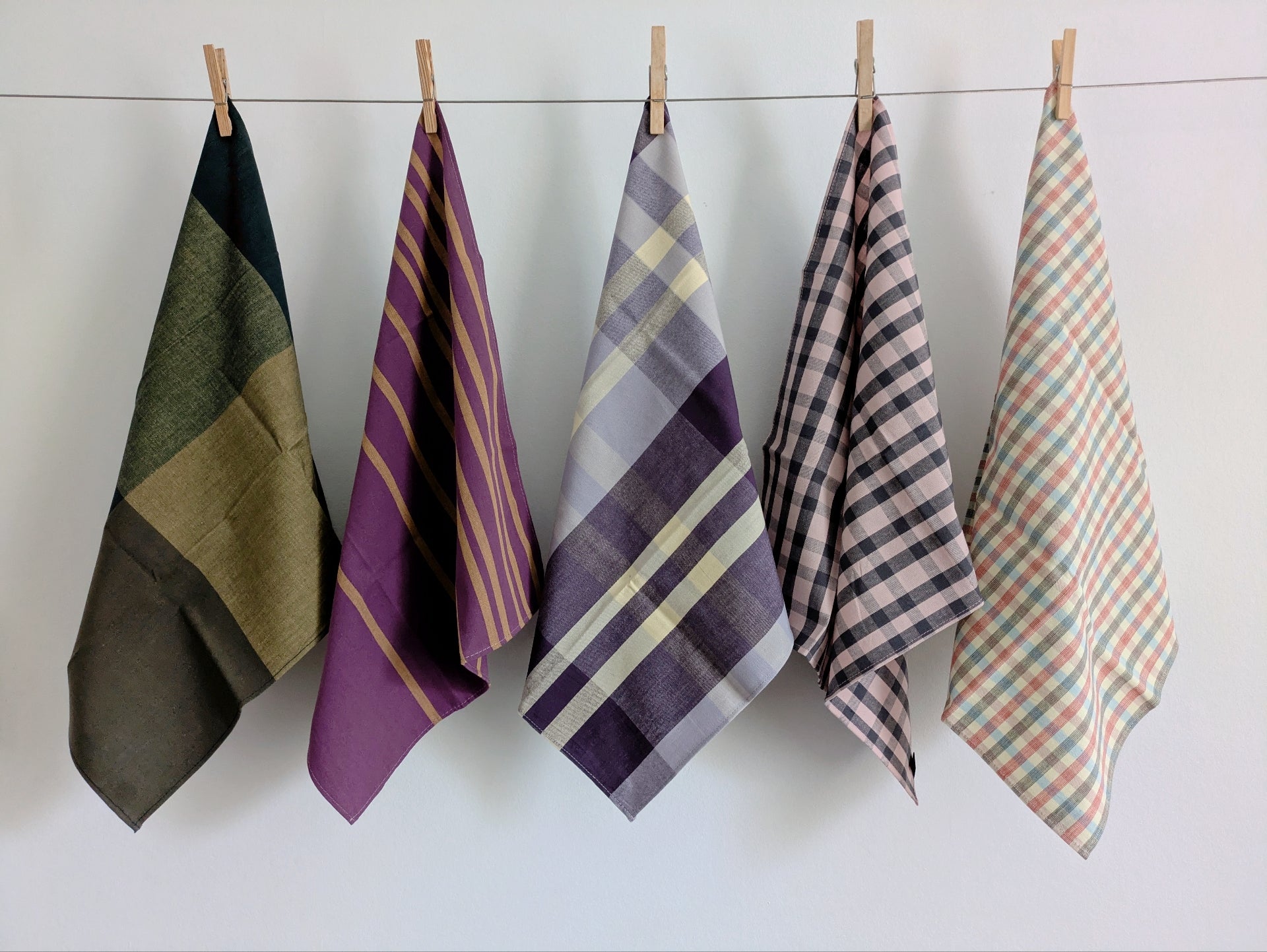 Five plaid towels hanging on a line against a white wall