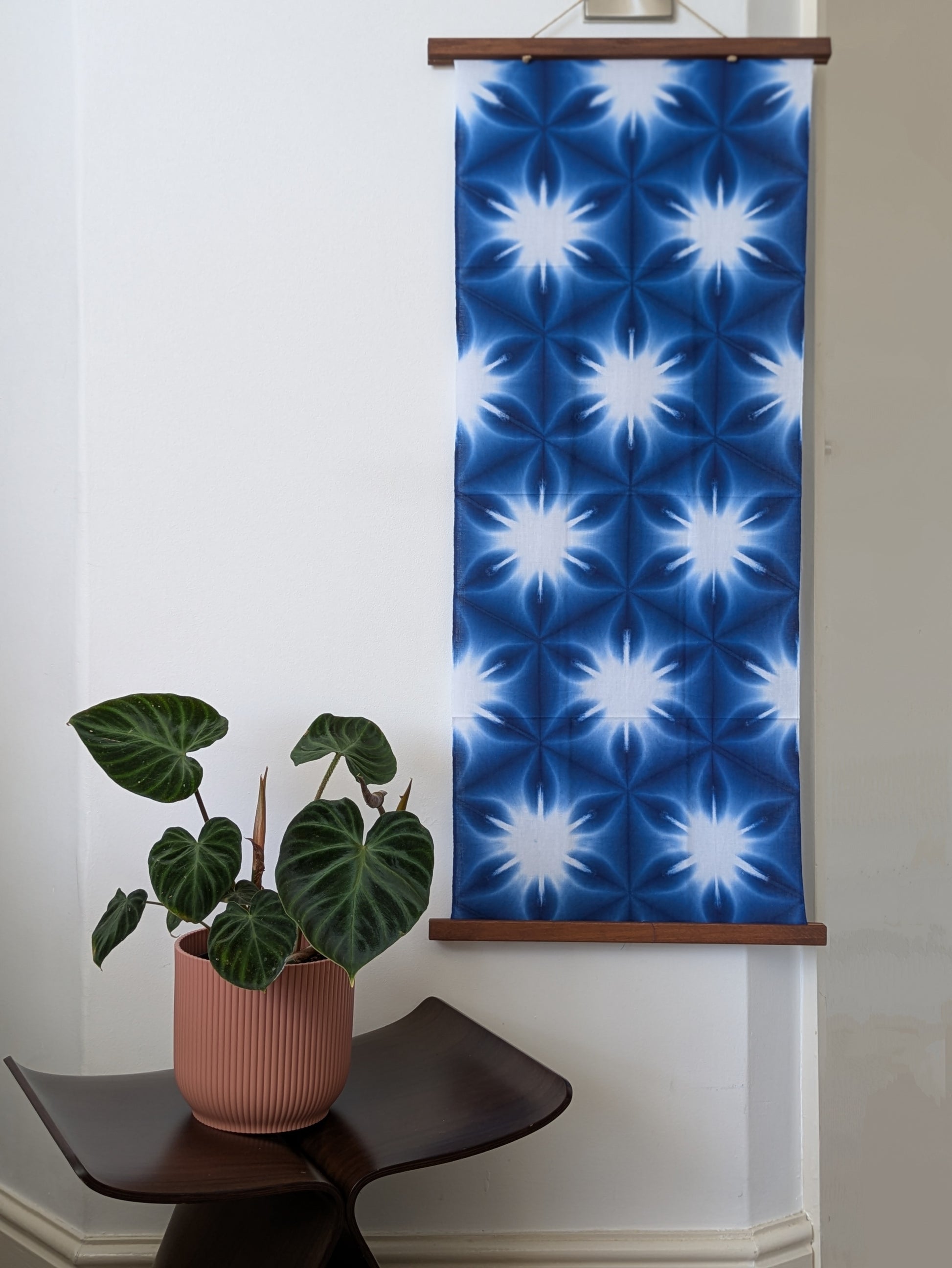 Blue and white patterned fabric hanging on a wall next to a plant.