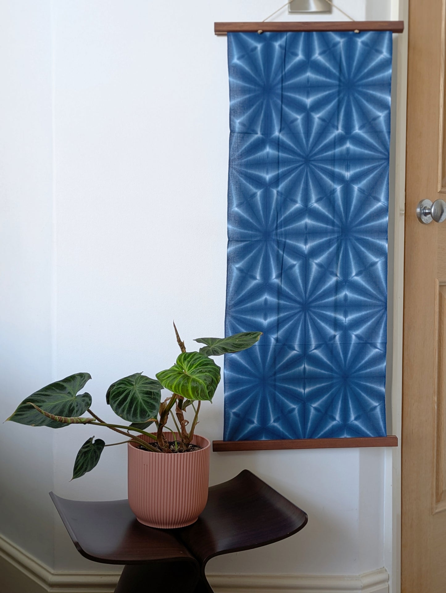 Blue geometric patterned fabric hanging on the wall with a plant and chair in the foreground.