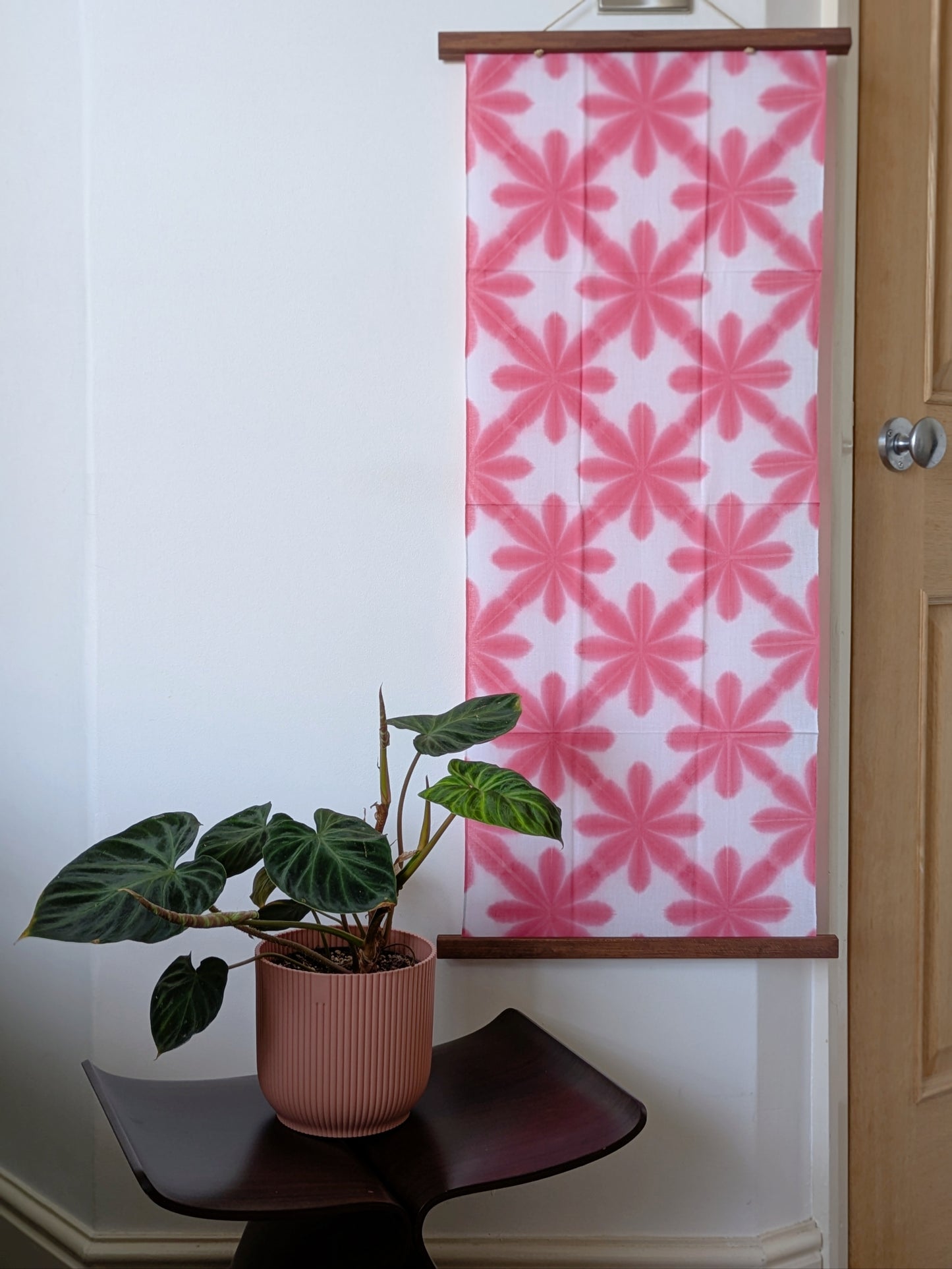 Pink floral patterned on a white wall with a plant on a chair below.
