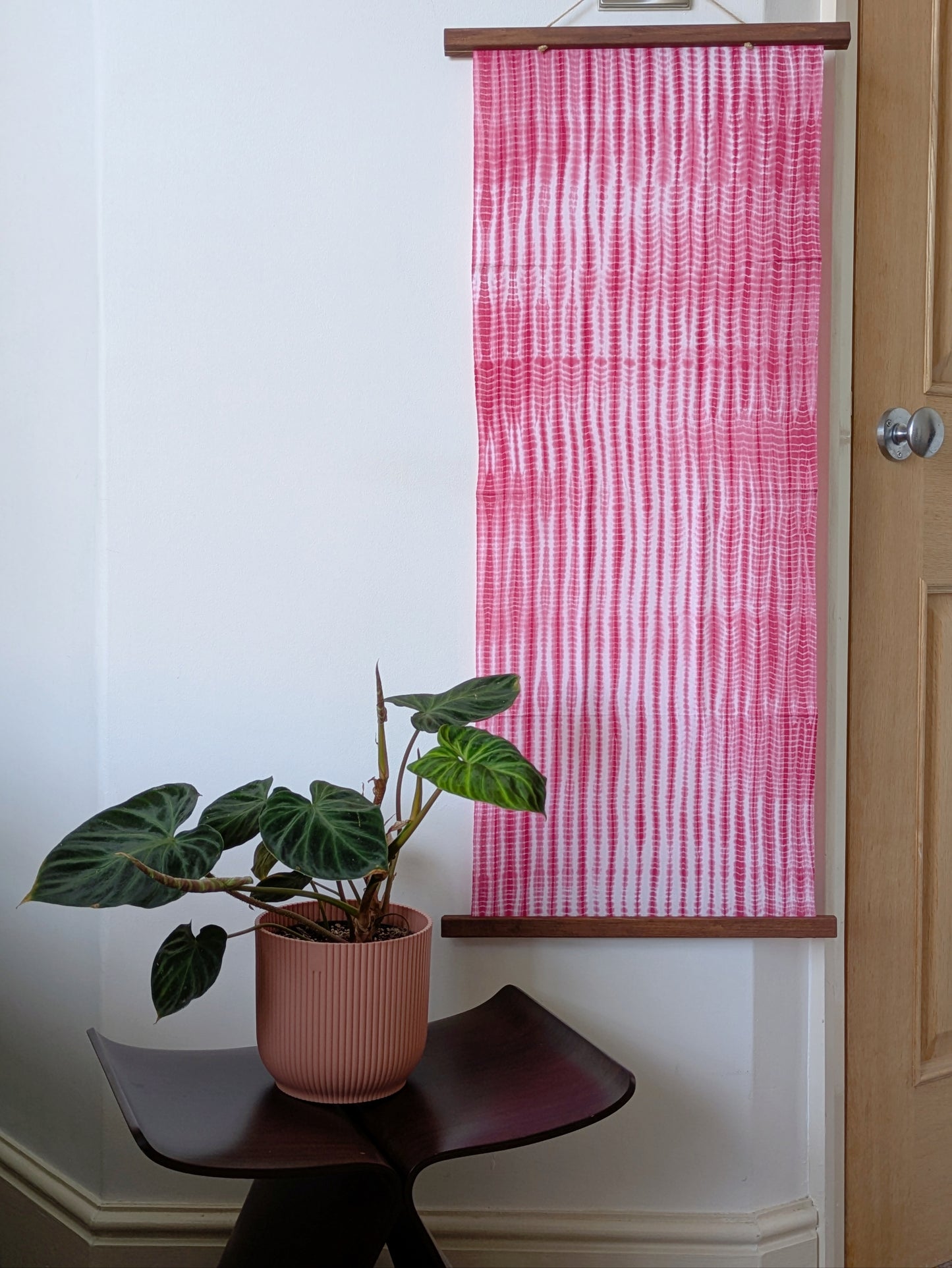 Pink and white striped fabric on the wall with a plant on a small chair.