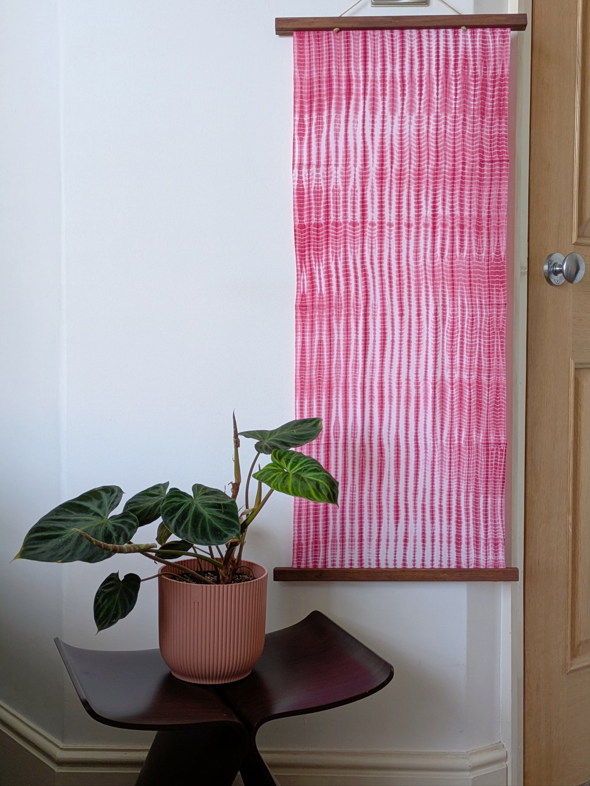 Pink and white striped fabric on the wall with a plant on a small chair.