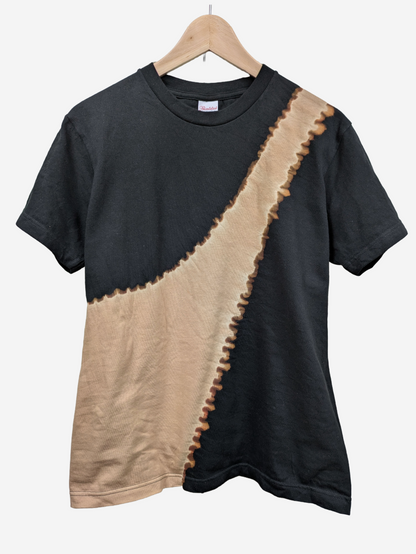 A black short-sleeve t-shirt with a diagonal beige tie-dye style panel and a frayed, scalloped brown edge, hanging on a wooden hanger against a light grey background.