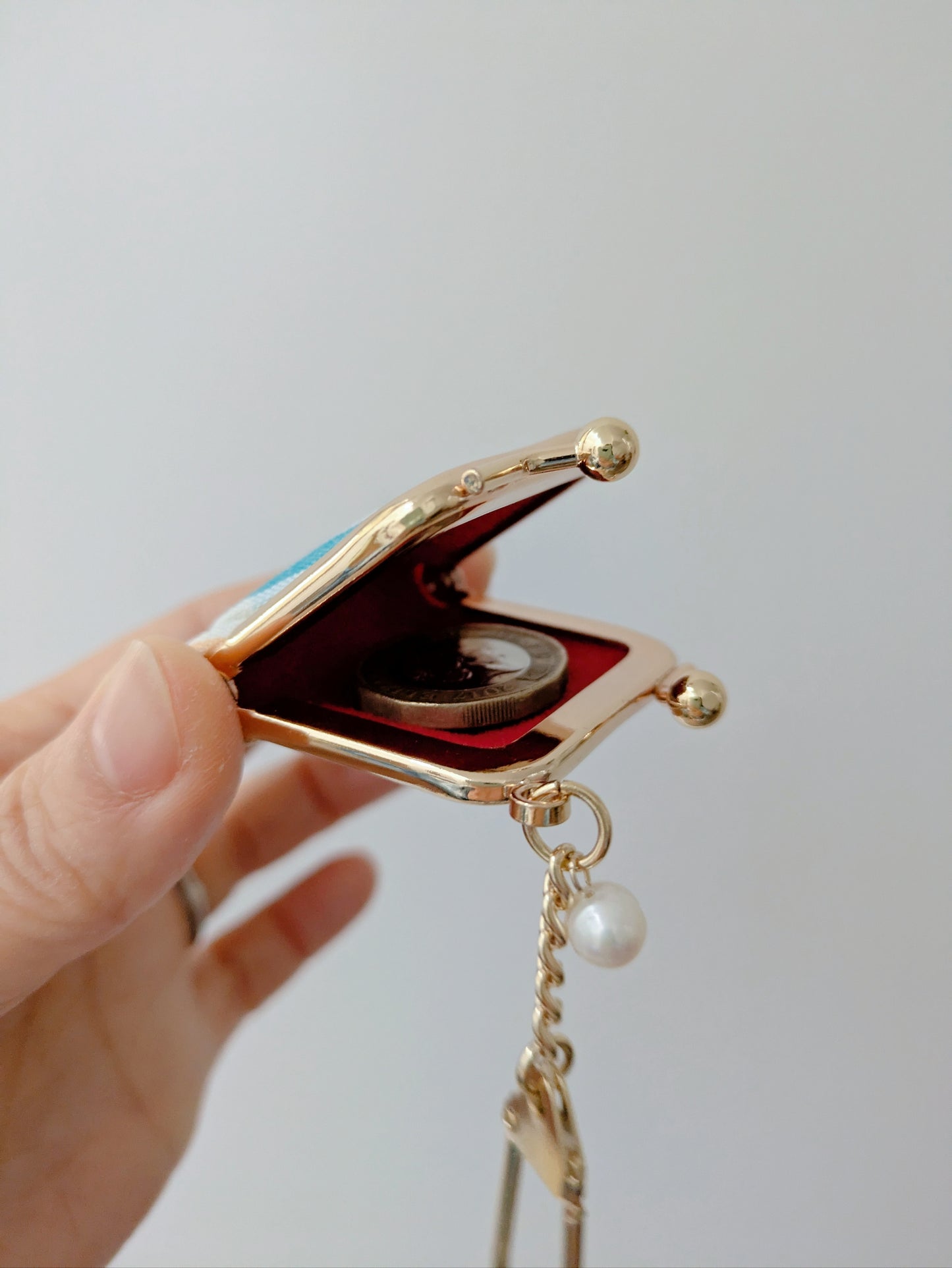 Gold jewelry box with a chain and pearl charm held by a hand against a light gray background