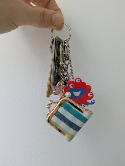 Keychain with striped pouch and colorful lion charm held by a hand on a white background