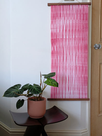 Pink and white striped fabric on the wall with a plant on a small chair.